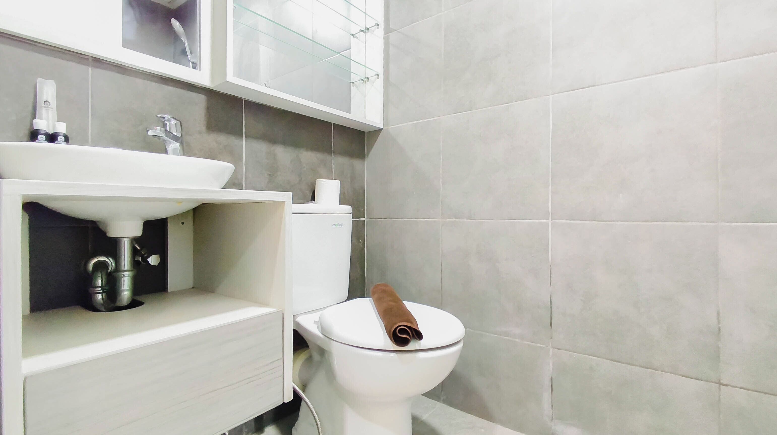 Een badkamer met een witte wastafel, een toilet en een glazen kast erboven.