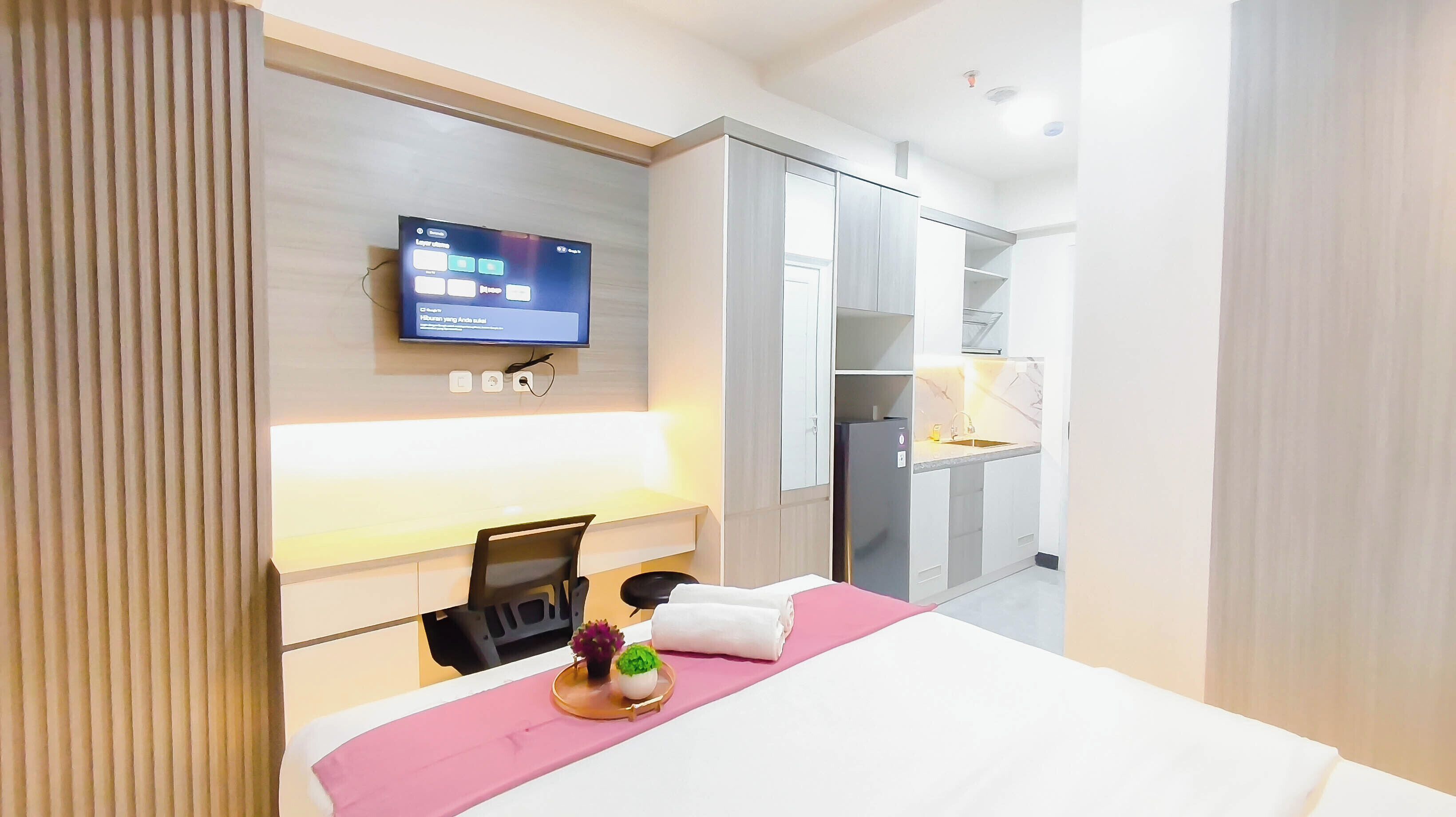 A hotel room with a bed, a TV mounted on the wall, a desk with a chair, and a wardrobe.