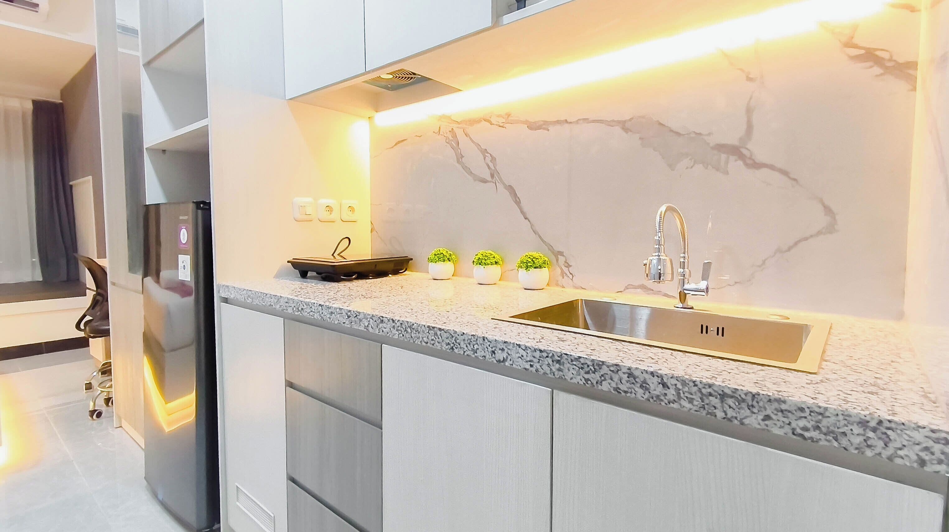 Una cocina moderna con salpicadero de mármol, un lavamanos de acero inoxidable y tres pequeñas macetas con plantas en la encimera.