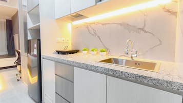 Una cocina moderna con salpicadero de mármol, un lavamanos de acero inoxidable y tres pequeñas macetas con plantas en la encimera.