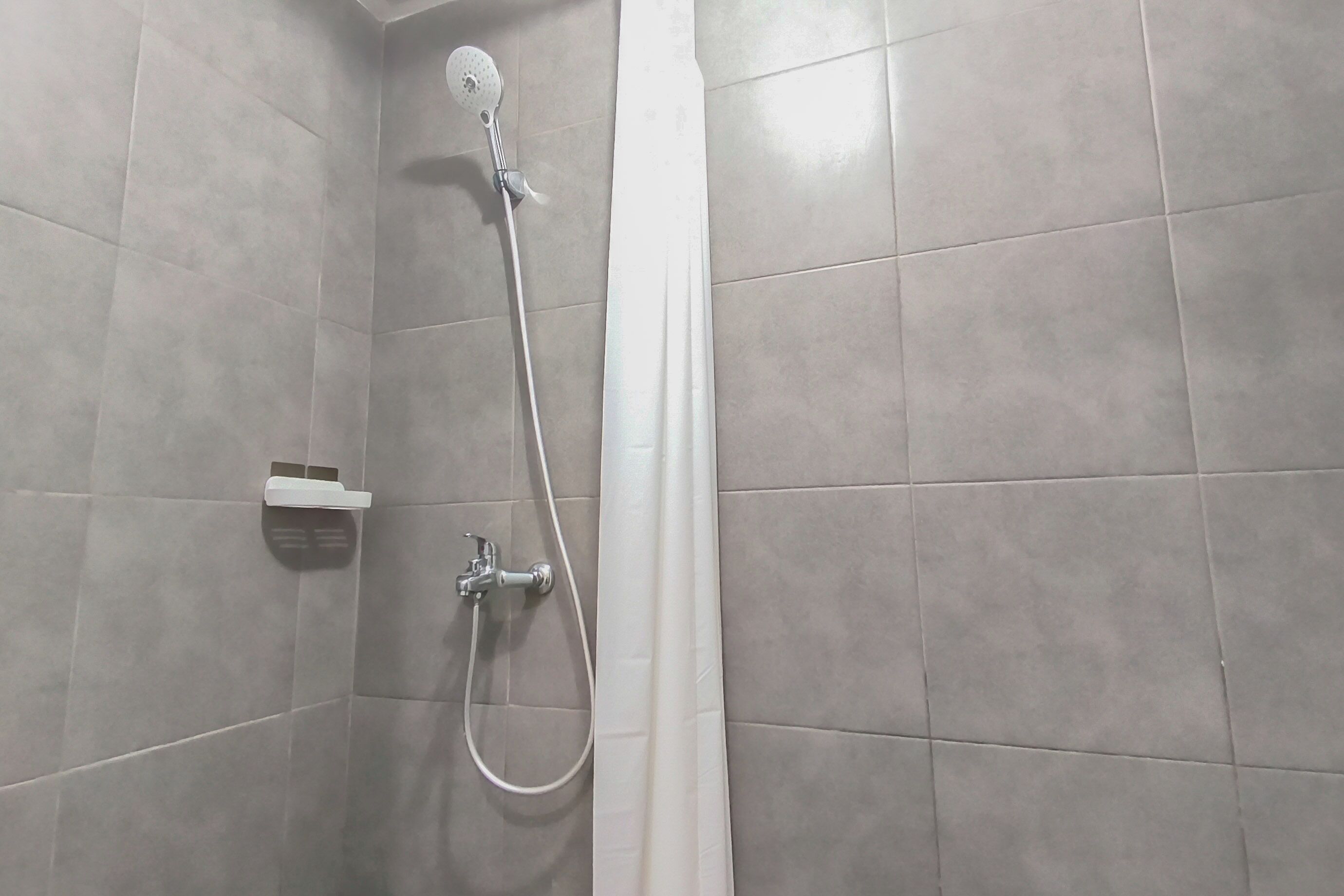 A shower area with a handheld showerhead, a wall-mounted faucet, and a white shower curtain.