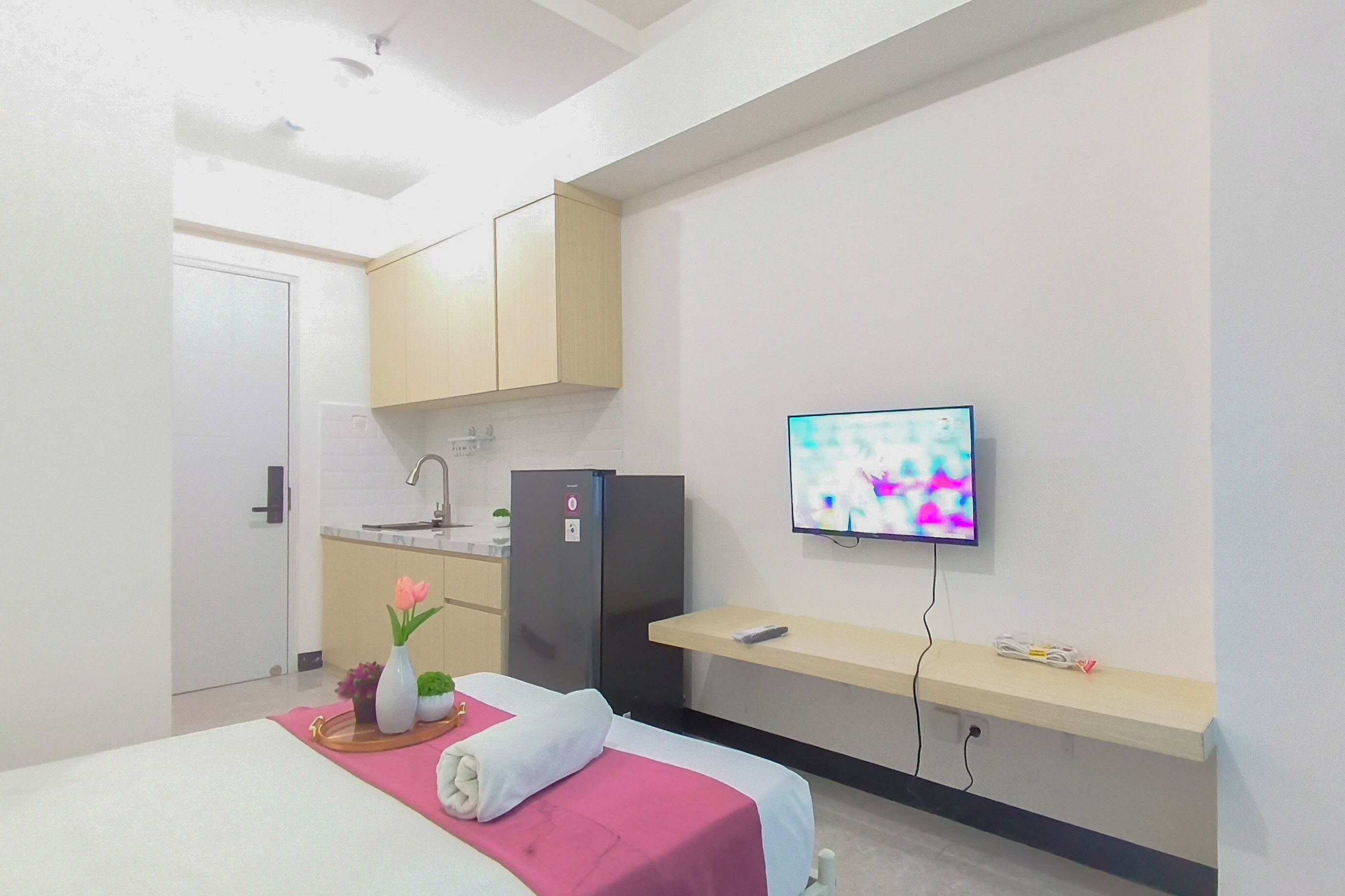 Une chambre d’hôtel avec un lit, un téléviseur fixé au mur, une petite kitchenette et une étagère en bois.