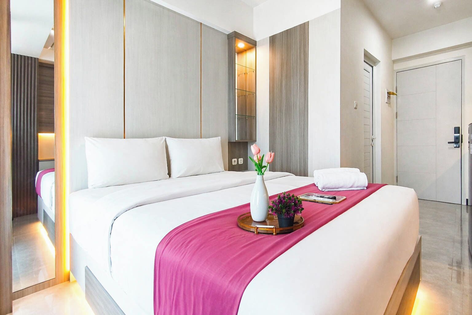 Una habitación de hotel moderna con una cama grande, una mesita de noche con un jarrón de flores y una manta roja.