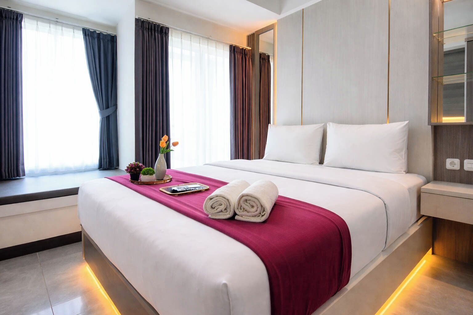 A hotel room with a large bed, a window with curtains, a bedside table, and a nightstand.