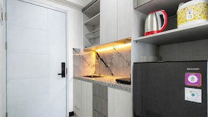 A compact kitchen with a built-in sink, a stainless steel kettle, and a refrigerator with a Sharp logo. - Serene Studio At Westown View Surabaya Apartment (Surabaya)