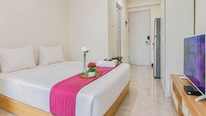 A hotel room with a bed, a TV, a tray with flowers, and a door leading to another room. - Pleasureable Studio Apartment At Westown View Surabaya (Surabaya)