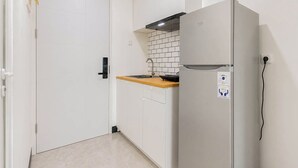 A compact kitchen with a refrigerator, a wooden countertop, and a tiled backsplash. - Pleasureable Studio Apartment At Westown View Surabaya (Surabaya)