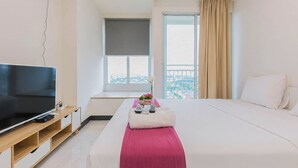 Habitación de hotel con cama, televisión, ventana con vistas y balcón.