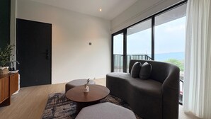 A modern living room with a sofa, ottoman, and coffee table, a wooden cabinet, and a large window with a view. - Guru Giri Forest Cabin Villa 2BR for 8 Pax (Include Breakfast) (Srimulyo)