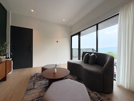 Una sala de estar moderna con sofá, puf y mesa de centro, un mueble de madera y un ventanal con vistas.