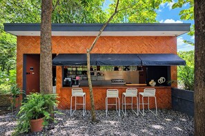 A modern outdoor bar area with a herringbone wood pattern, a black awning, and four white bar stools. - 2Br For 8Pax At Guru Giri Forest Cabin Villa (Include Breakfast) (Srimulyo)
