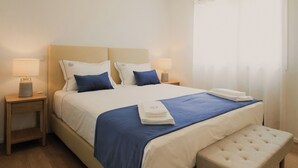 Ein ordentlich eingerichtetes Hotelzimmer mit einem großen Bett, Nachttischen, einer Bank und einem Fenster mit Vorhängen.