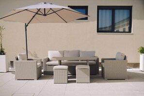Een terras met een zithoek, poefjes en een grote parasol.