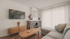 Ein modernes Wohnzimmer mit Kamin aus Stein, einem Flachbildfernseher, einem Holztisch und einem beigefarbenen Sofa.