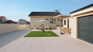 Ein modernes Haus mit Terrasse, Gartenmöbeln und Garage.