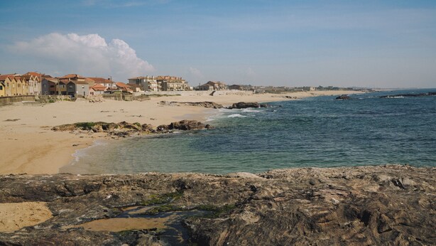 Eine Küstenlandschaft mit Gebäuden, einem Sandstrand und felsiger Küstenlinie.