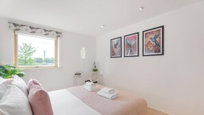 Ein Schlafzimmer mit Bett, Kissen, einem Fenster, einem Nachttisch und Wandbildern.