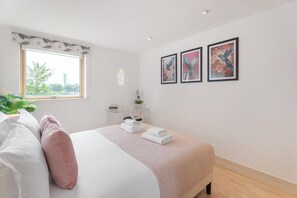 Ein Schlafzimmer mit Bett, Kissen, einem Fenster, einem Nachttisch und Wandbildern.