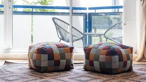 Ein Balkon mit zwei schwarzen Stühlen aus Draht und zwei farbenfrohen, karierten Hocker auf einem gemusterten Teppich.