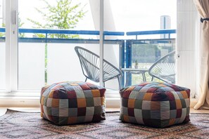 Ein Balkon mit zwei schwarzen Stühlen aus Draht und zwei farbenfrohen, karierten Hocker auf einem gemusterten Teppich.