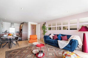 Ein modernes Wohnzimmer mit einem blauen Sofa, einem Esstisch mit Stühlen, einer roten Lampe und einem gemusterten Teppich.