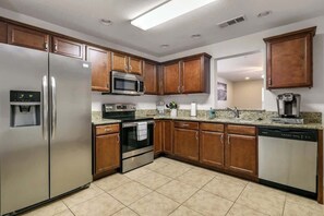 Una cocina moderna con electrodomésticos de acero inoxidable, armarios de madera y piso de baldosas.