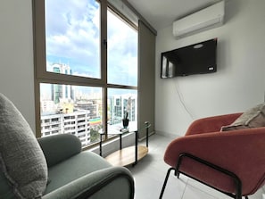 Ein modernes Wohnzimmer mit großem Fenster, Flachbildfernseher und Blick auf eine Stadtlandschaft.
