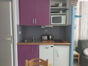 A compact kitchen with purple cabinets, a white microwave, a Siemens dishwasher, and a small table with a kettle. - T1 cabine pour 4 avec terrasse piscine l'été (ARZON)