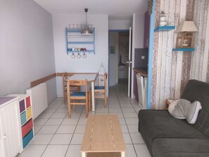A compact living space with a dining table, chairs, a sofa, a kitchen area, and a radiator. - T1 cabine pour 4 avec terrasse piscine l'été (ARZON)