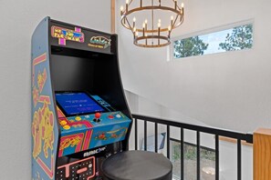 A retro arcade machine with a colorful interface, a black stool, and a chandelier in a room with a balcony view.