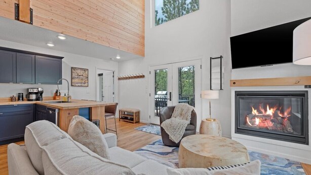 A modern living room with a fireplace, a sofa, a coffee table, and a kitchen area with a dining table. - Cloudview Lodge  Retreat (Rapid City)