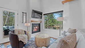 A modern living room with a fireplace, a television, and a view of trees. - Cloudview Lodge  Retreat (Rapid City)