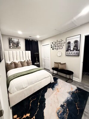 Ein modernes Schlafzimmer mit einem großen Bett, einer Sitzbank, einer Wanduhr und einem gerahmten Bild.