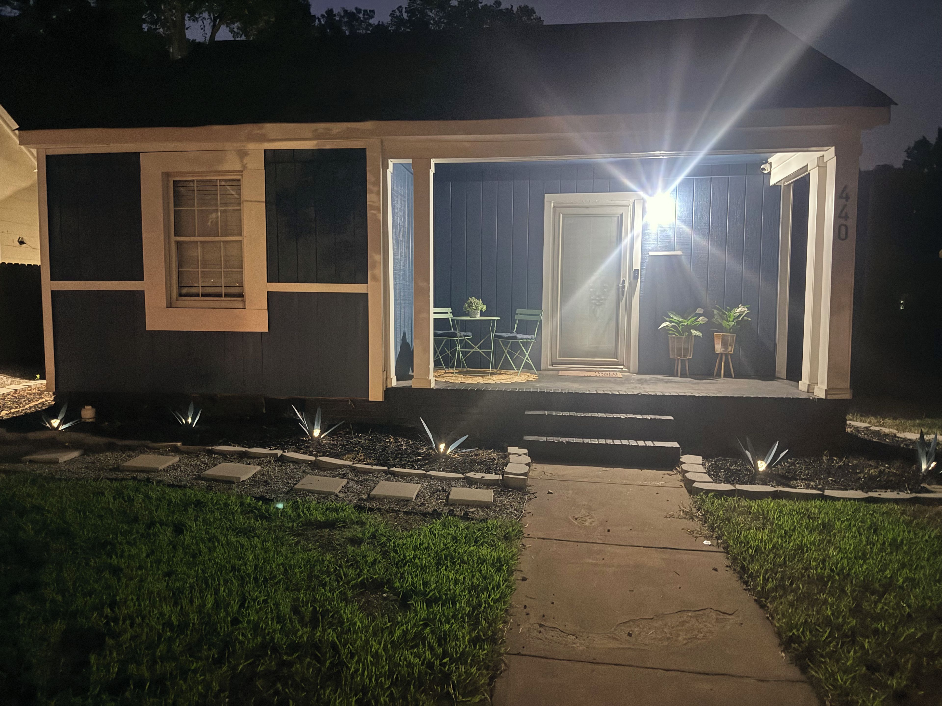 Une maison d’habitation avec un porche à l’avant, une porte et un petit espace extérieur aménagé avec une table et des chaises.