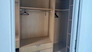 Un dressing accessible sans porte, doté d’étagères ouvertes, d’une tringle et d’un seul tiroir.