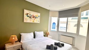 Une chambre à coucher comprenant un lit, deux tables de chevet, une fenêtre avec vue, un radiateur et un tableau accroché au mur.