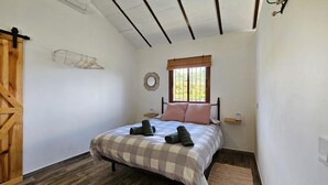 A bedroom with a bed, a wooden door, a window with a view, a wall-mounted mirror, and a bedside table. - Amazing home in Yunquera (Yunquera)