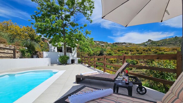A poolside area with a lounge chair, a table with a bottle, and a view of a hillside. - Amazing home in Yunquera (Yunquera)