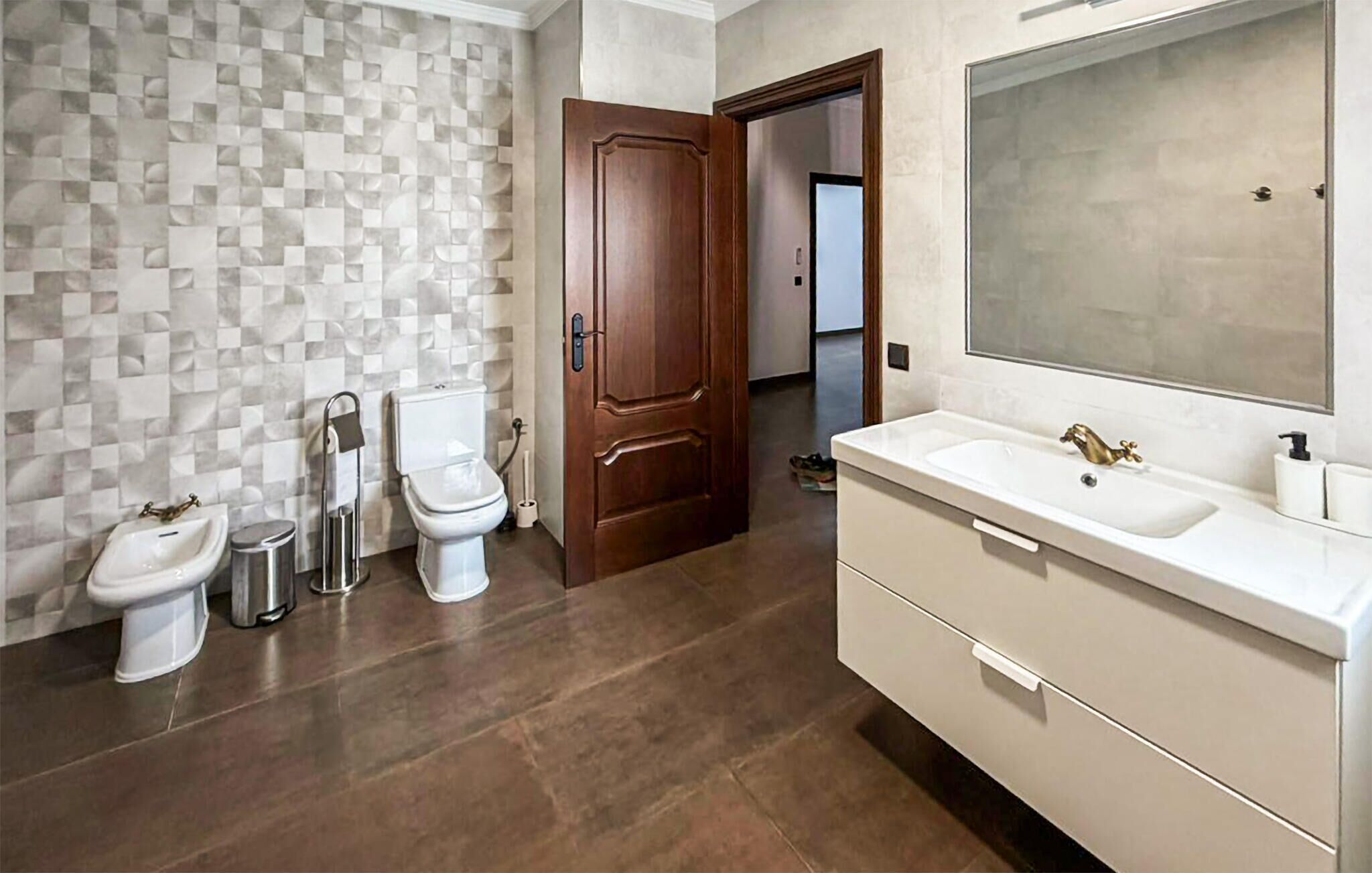 Une salle de bain avec un mur carrelé, une porte en bois, un lavabo blanc et un miroir.