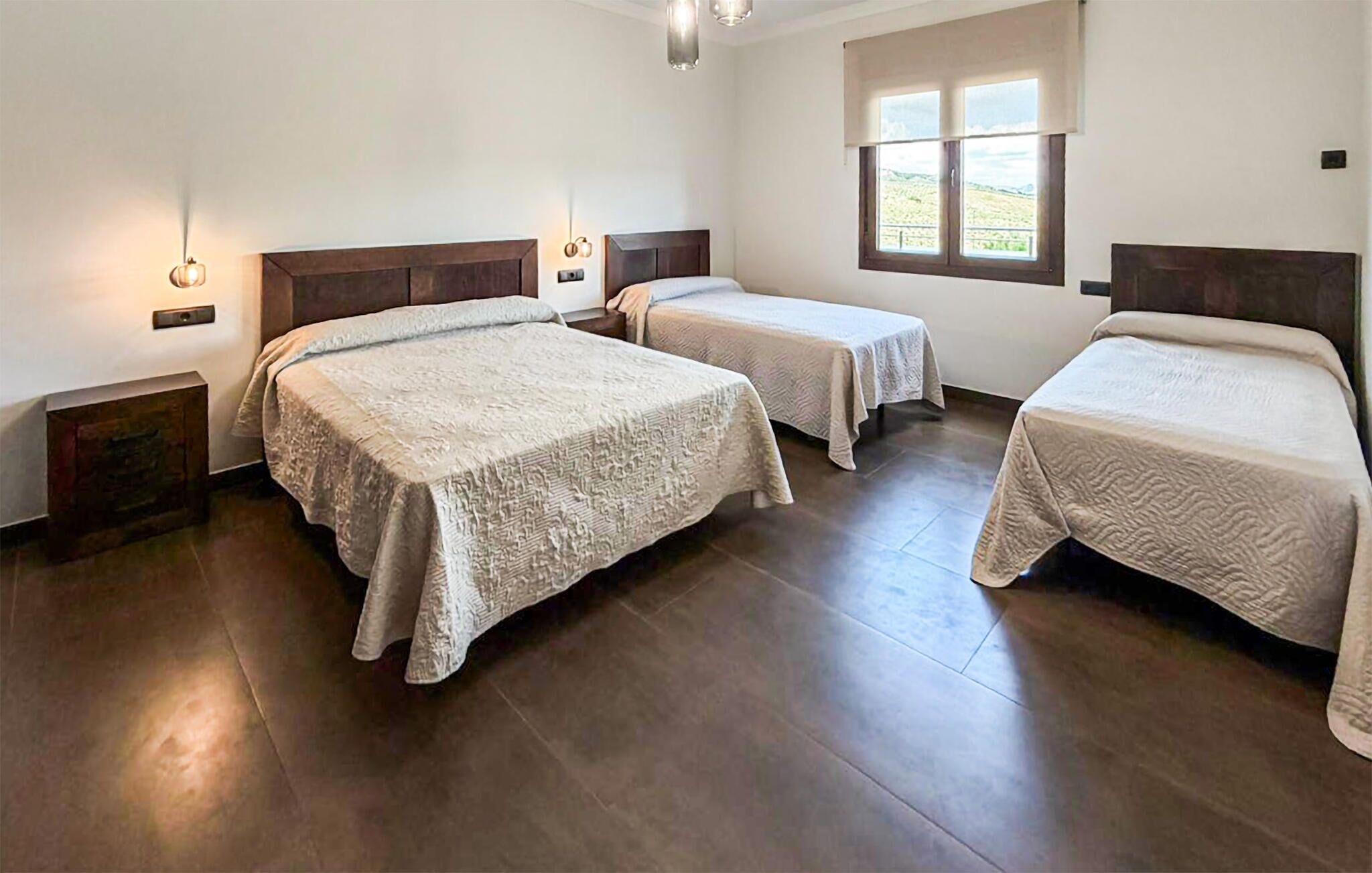 Una habitación de hotel con tres camas, un ventanal con vistas y suelo de madera.
