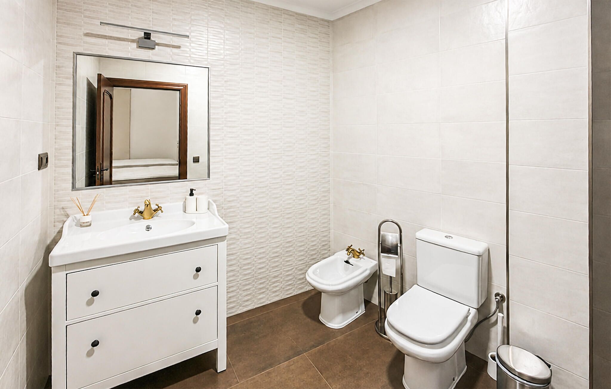 A bathroom with a white vanity, a mirror, a bidet, a toilet, and a trash can.