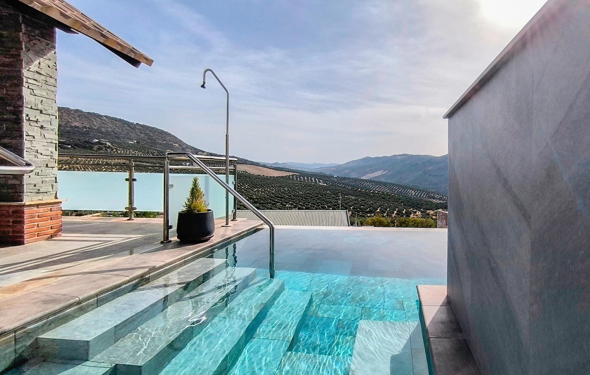 A swimming pool with steps leading down to the water, a potted plant, and a view of distant mountains.