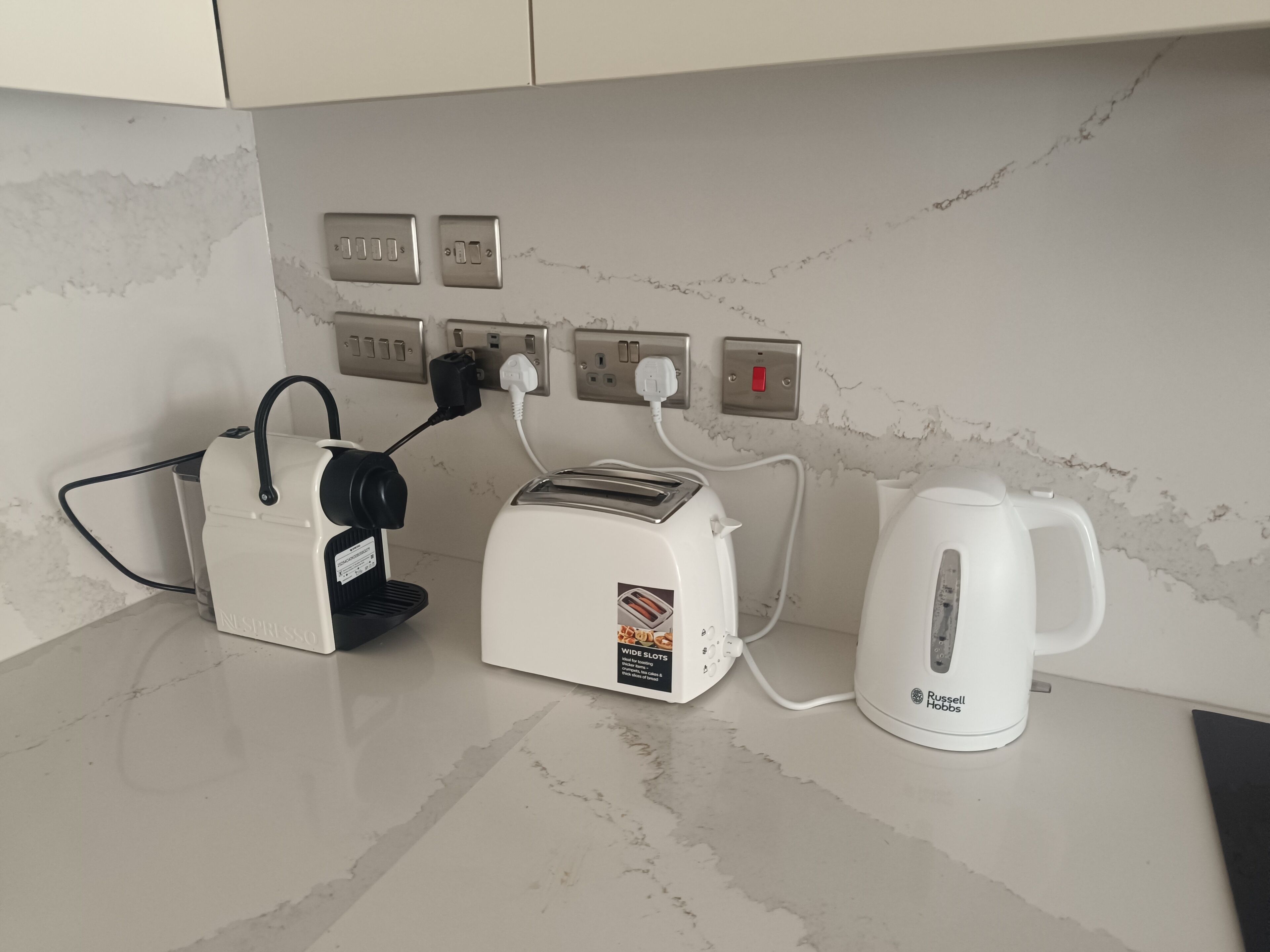 Una cocina con cafetera, tostadora y hervidor sobre una encimera de mármol.