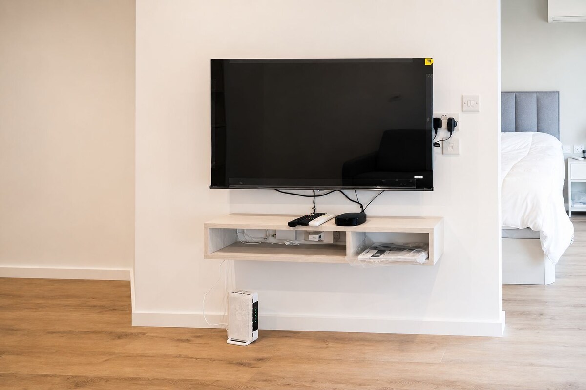 Una sala de estar moderna con un televisor de pantalla plana montado en la pared, un mueble de entretenimiento de madera debajo y una consola blanca.