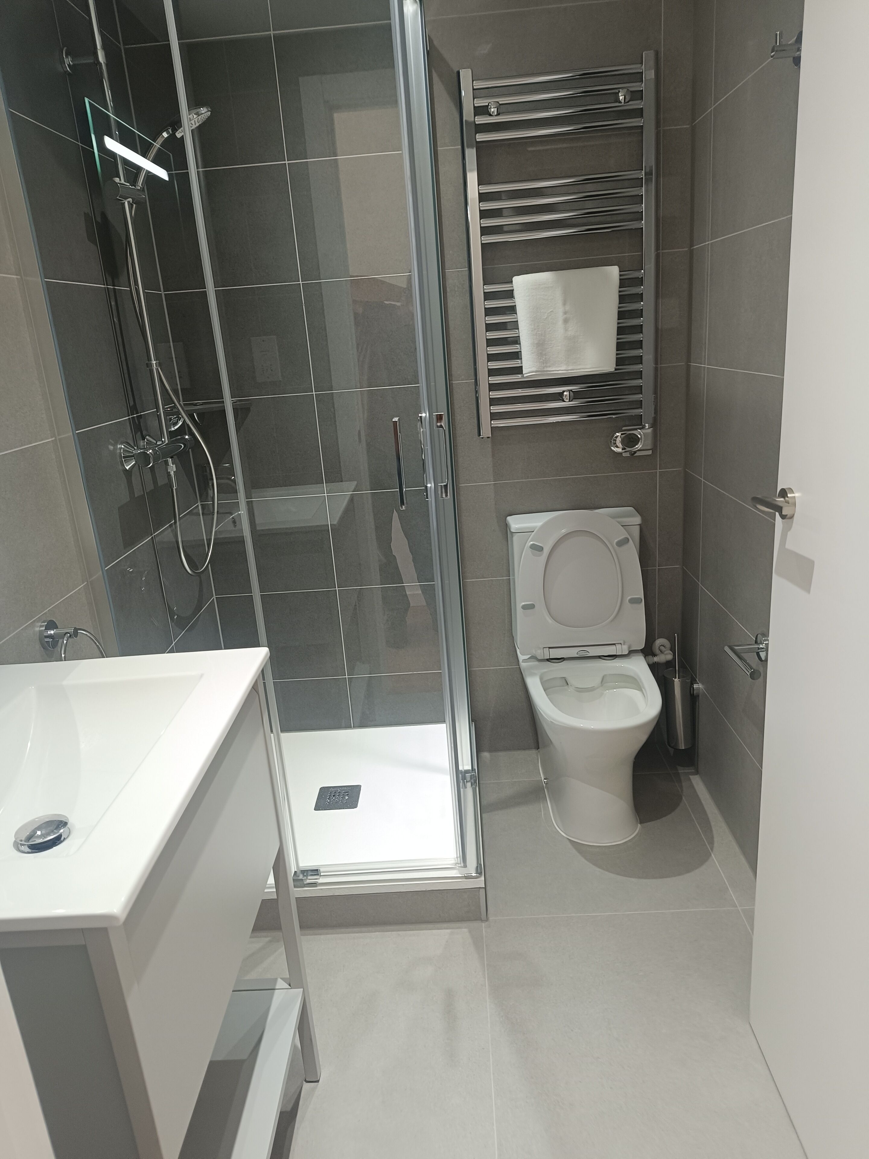 Un baño moderno con cabina de ducha de vidrio, inodoro blanco y lavamanos con espejo.