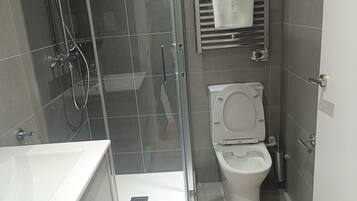 Un baño moderno con cabina de ducha de vidrio, inodoro blanco y lavamanos con espejo.