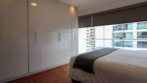 Ein Schlafzimmer mit einem großen Bett, einem Kleiderschrank und Blick auf ein Gebäude durch ein Fenster.