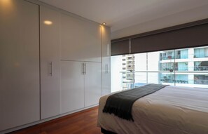 A bedroom with a large bed, a wardrobe, and a view of a building through a window. - w* | Deluxe 3BR Duplex w/ Balcony in Miraflores (Lima)