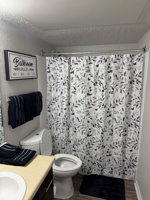 Ein Badezimmer mit Toilette, Waschbecken und Duschvorhang mit Blättermotiv.