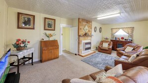 Een woonkamer met een open haard, leren banken, een houten kast en ingelijste foto's aan de muur.